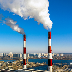 Red and white smokestacks spewing smoke against a blue sky